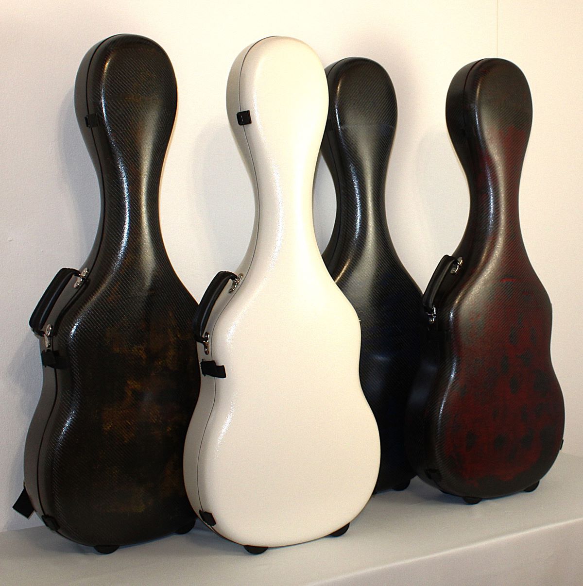 Four carbon fiber guitar cases in different colors on a white background