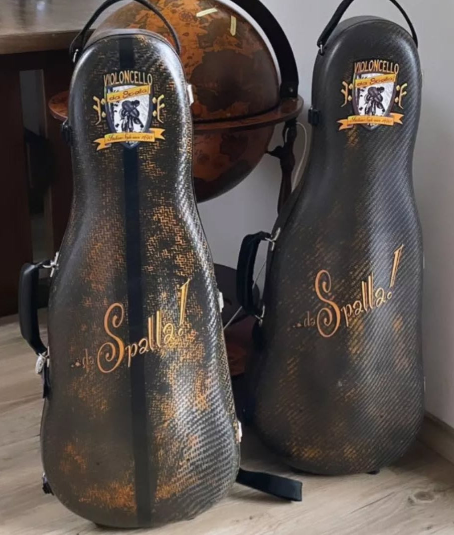 Two cello da spalla cases with branding on a wooden floor