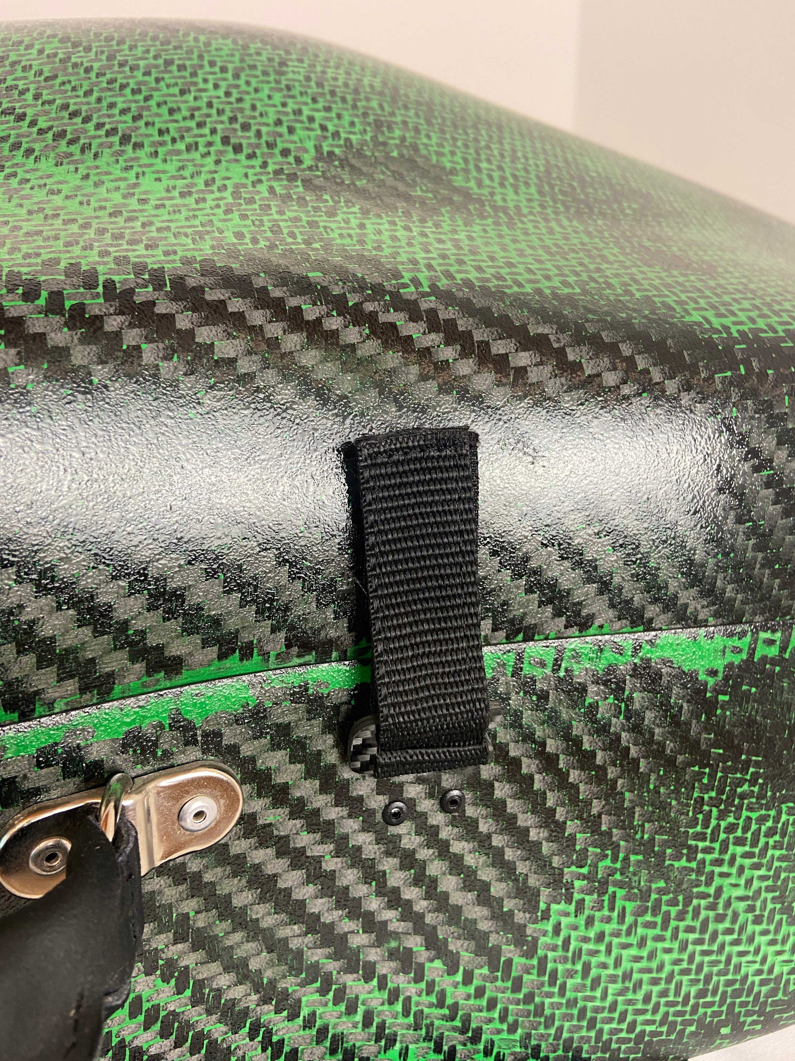 Close-up of a green and black viola da gamba case with a black velcro strap and metal clip.
